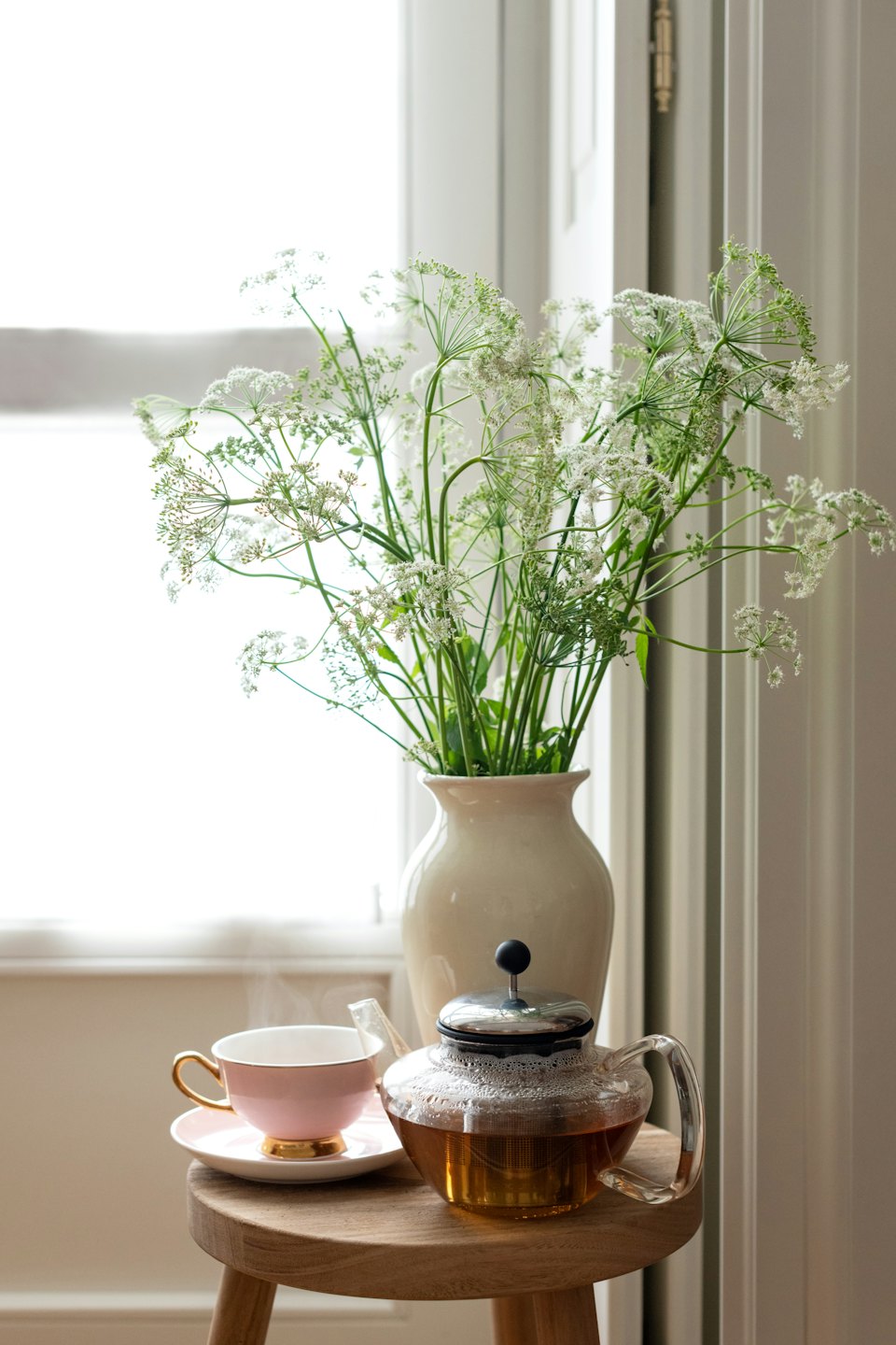 Glass teapot and teacup on a wooden stool with flowers.