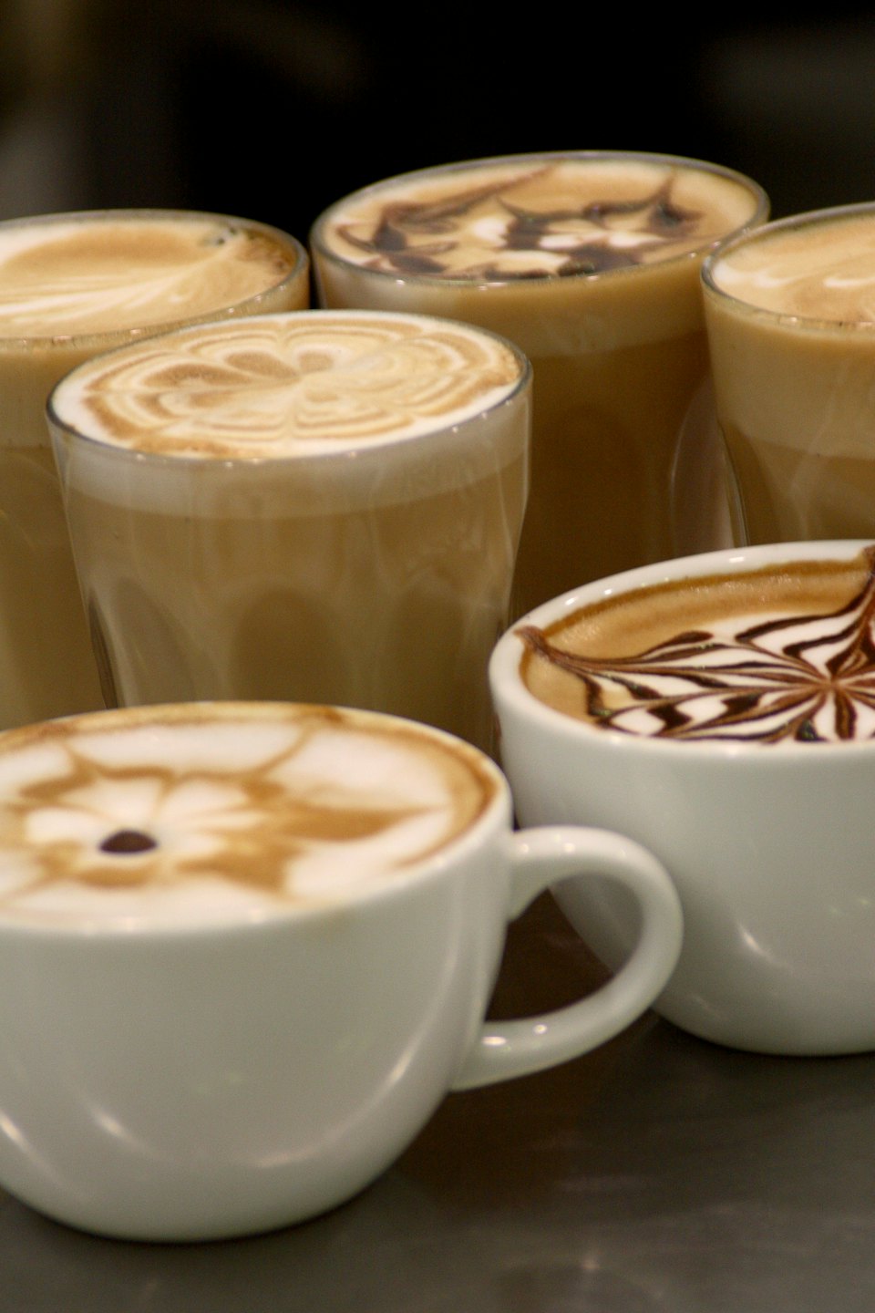 Various coffee drinks with latte art sit on a table.