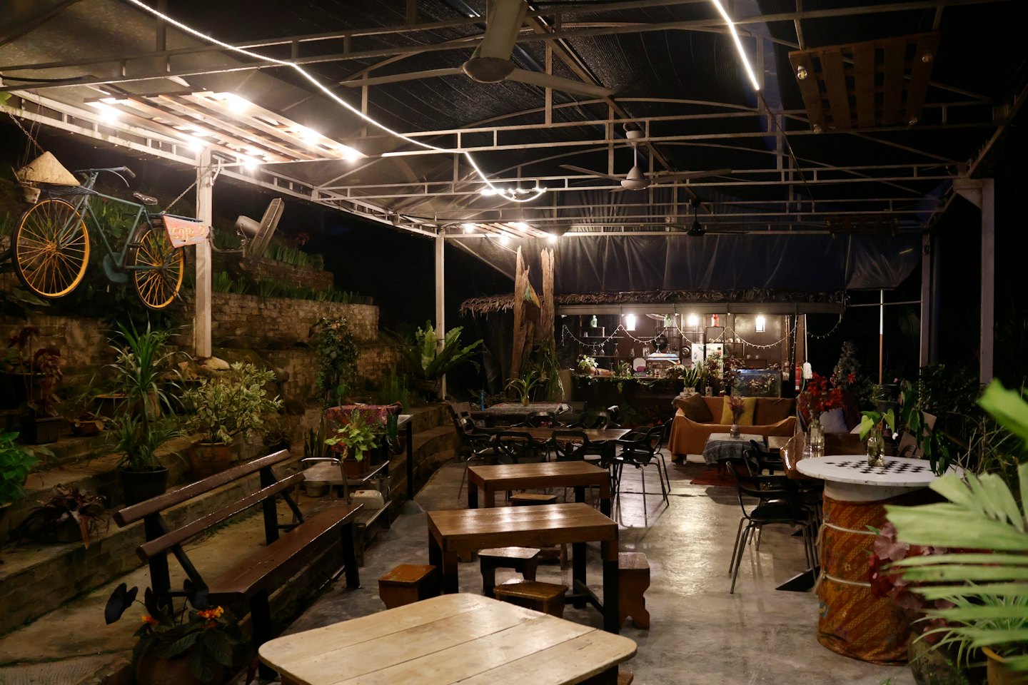 Outdoor cafe patio with wooden tables and decorative string lights.