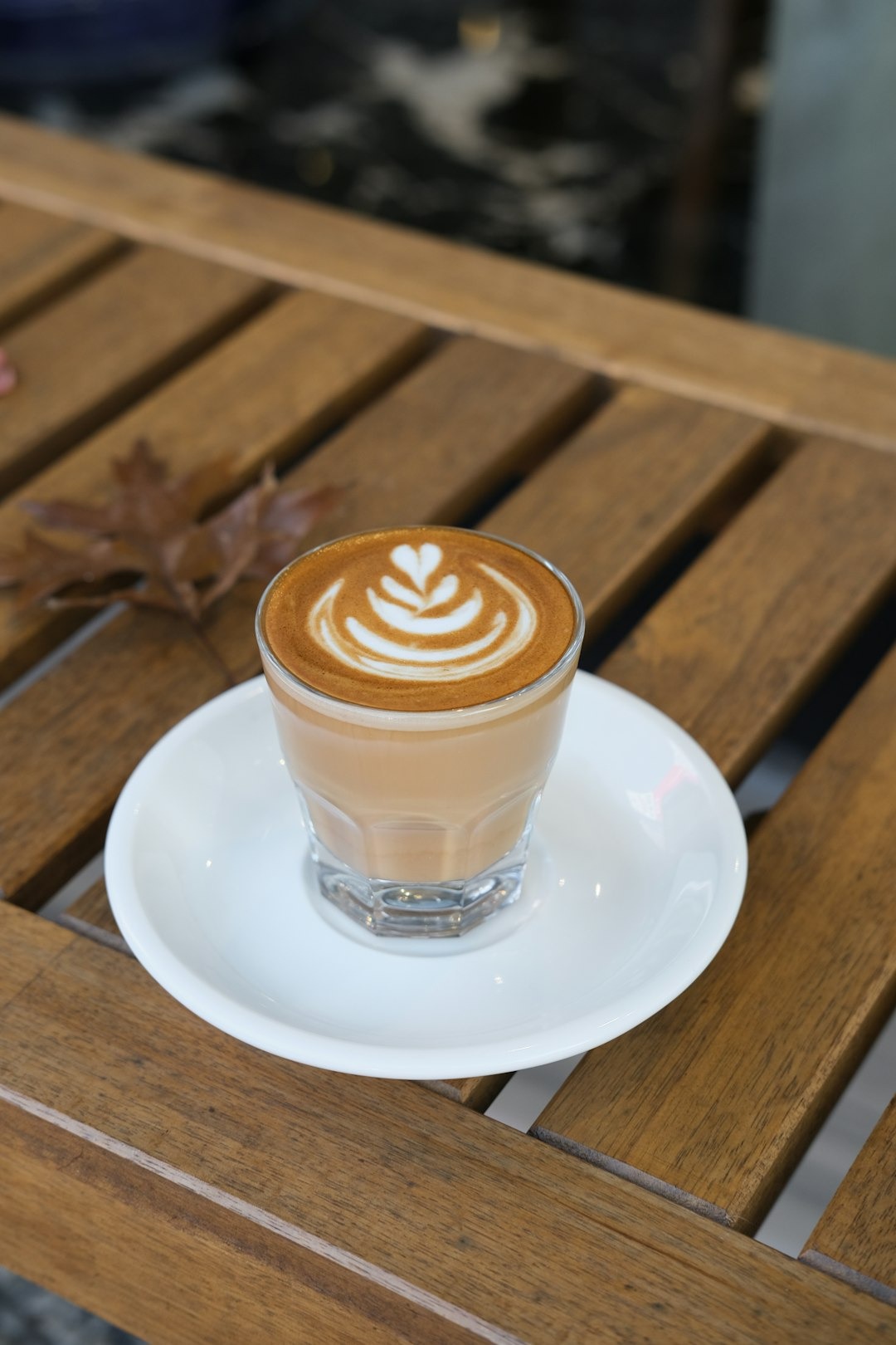 A glass of latte with foam art sits on a wooden table.
